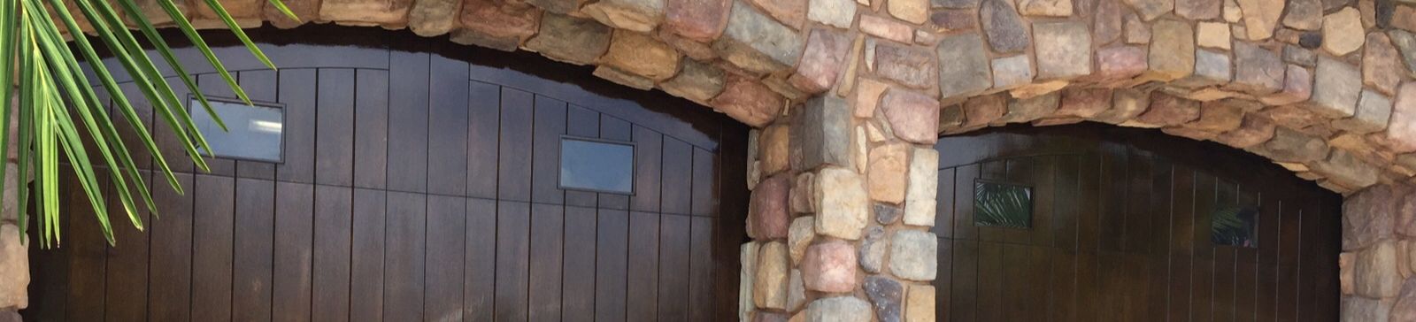 Two newly installed dark wood-style garage doors with vertical panels and arched tops on a stone façade home in Casselberry, FL.