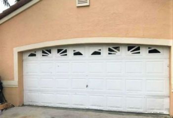 Old white garage door with decorative windows and visible wear on a peach-colored Casselberry home.