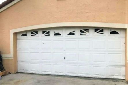 Old white garage door with decorative windows and visible wear on a peach-colored Casselberry home.