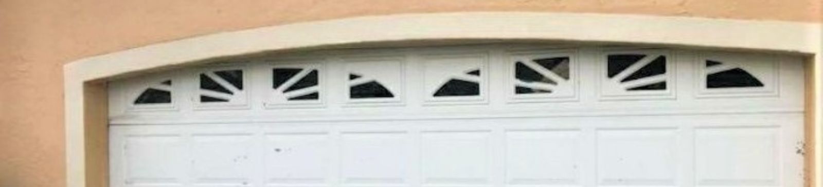 Old white garage door with decorative windows and visible wear on a peach-colored Casselberry home.