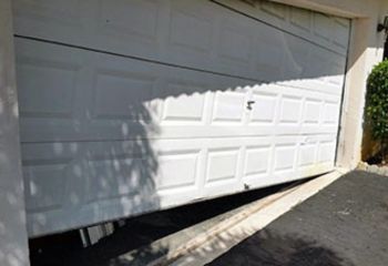 White sectional garage door off its tracks and tilted at an angle, showing severe misalignment and roller failure at a Fern Park, FL home.