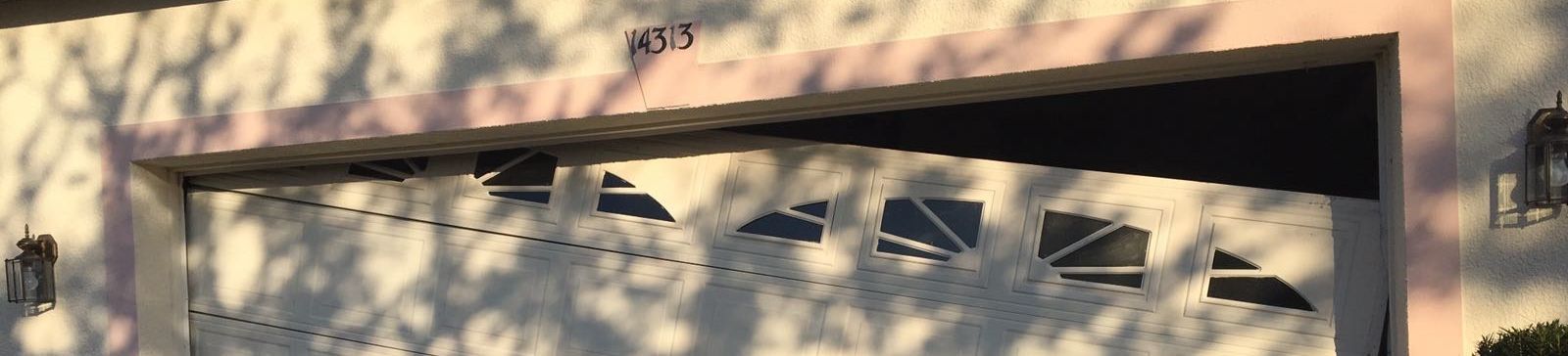 White sectional garage door off-track and hanging at an angle due to a damaged and rusty vertical track on a Longwood home.