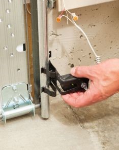 Technician adjusting a new black photoelectric safety sensor on a metal garage door track in an Altamonte Springs home.