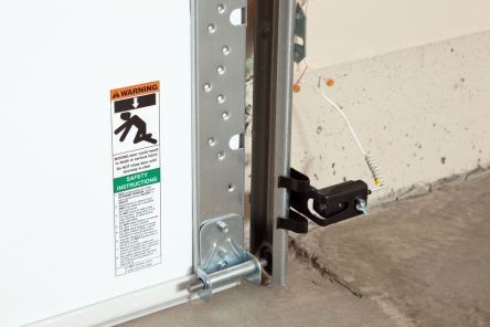Side view of a garage door track and safety sensor, showing a green indicator light and secure mounting for reliable electric garage door operation.
