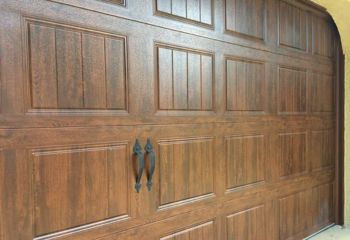 Close-up of a newly installed wood-look garage door with vertical panels and black decorative handles on a Longwood, FL home.